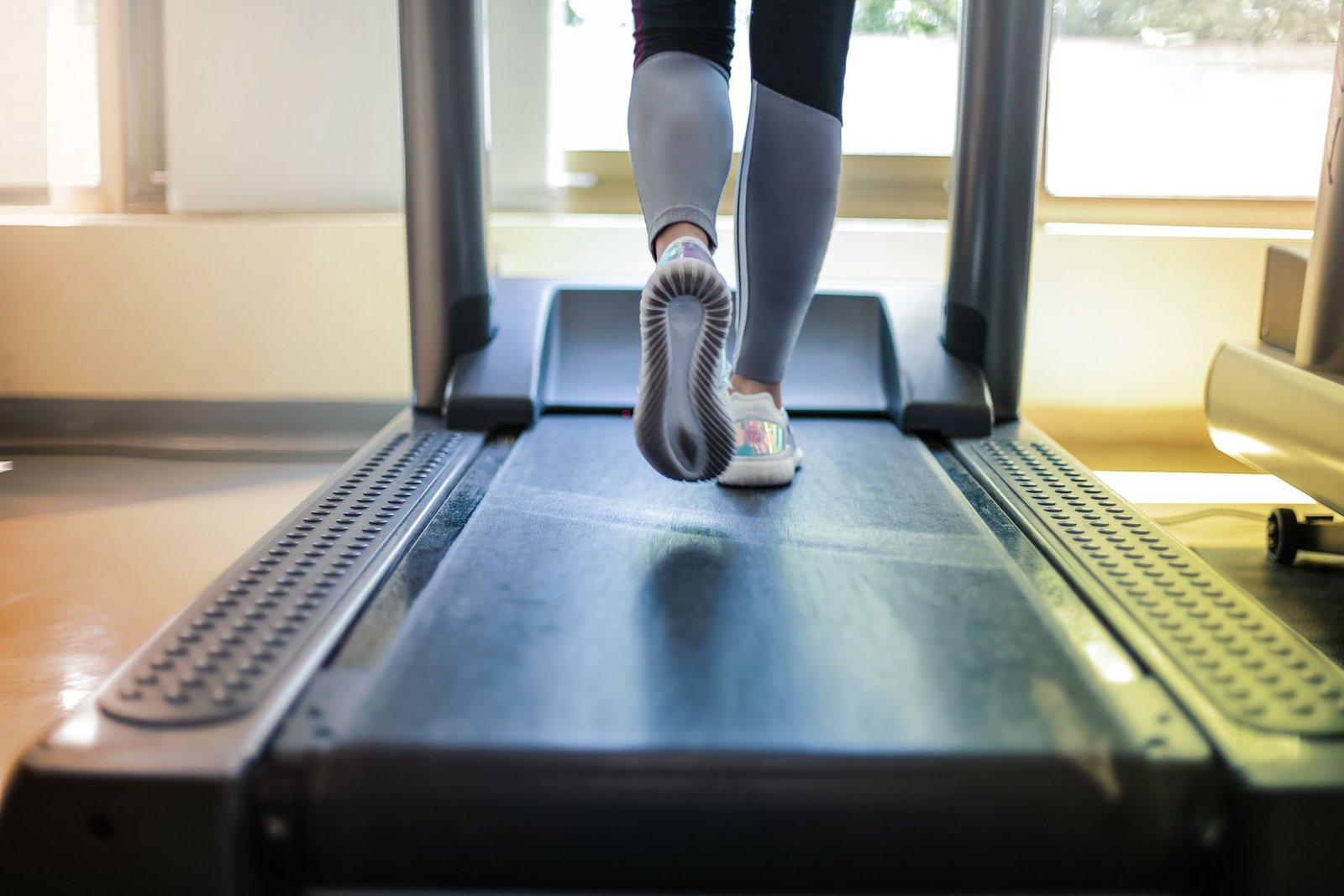 Close-up of feet walking on a treadmill belt beside a bright window