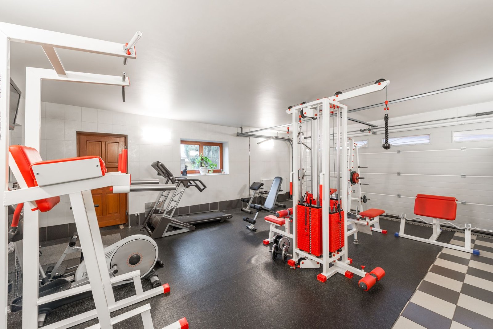 A home gym with a treadmill, weight bench and dumbbells in a garage
